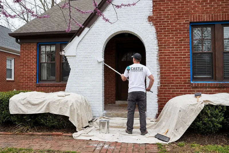Painter rolling white paint on a brick entry arch.