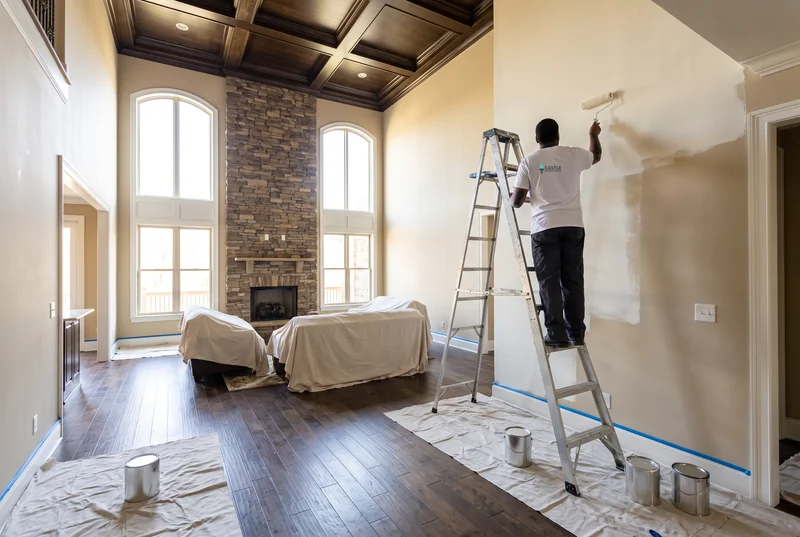 Painter on a tall ladder painting a two-story great room with stone fireplace