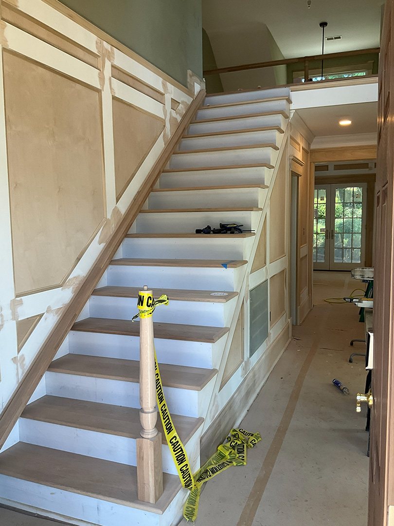 Primed stair railing and wainscot with caution tape during an interior paint job