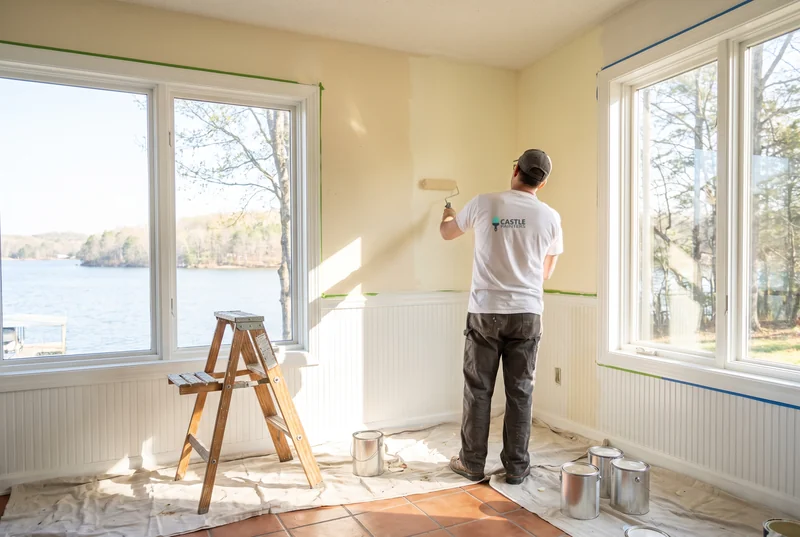 Painter rolling warm white paint above beadboard in a lake-view sunroom