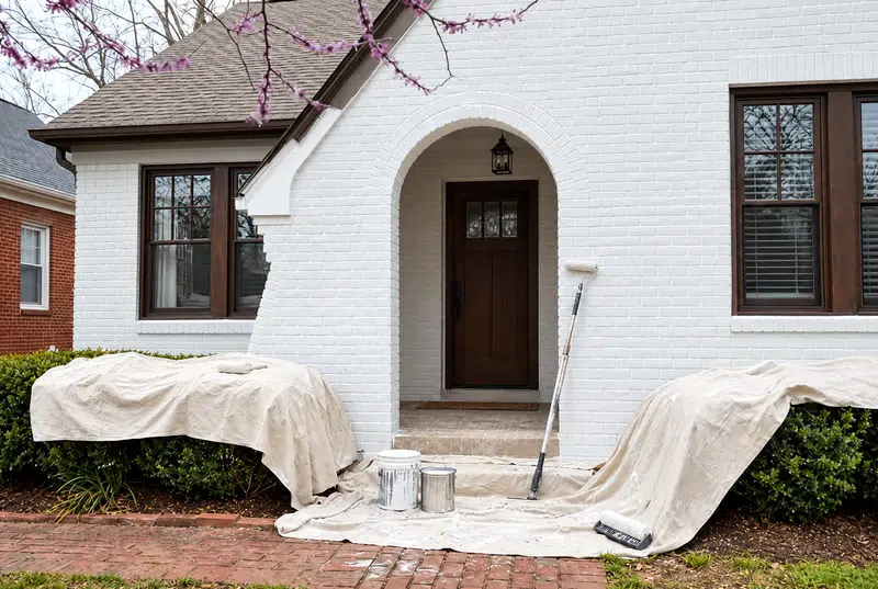 Brick home freshly painted white with drop cloths in place, brick painting in Knoxville, TN by Castle Painters