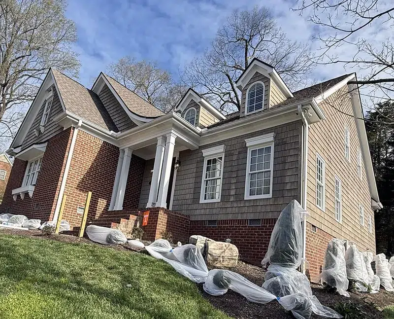 Brick and cedar shake home with shrubs wrapped in plastic before exterior painting, house painting FAQ in Knoxville, TN